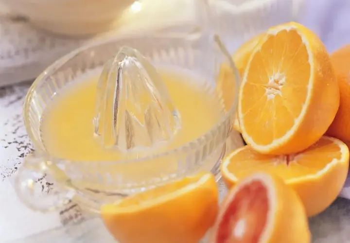 Exprimiendo naranjas frescas en un exprimidor de vidrio. El zumo de naranja natural recién hecho, listo para disfrutar.
