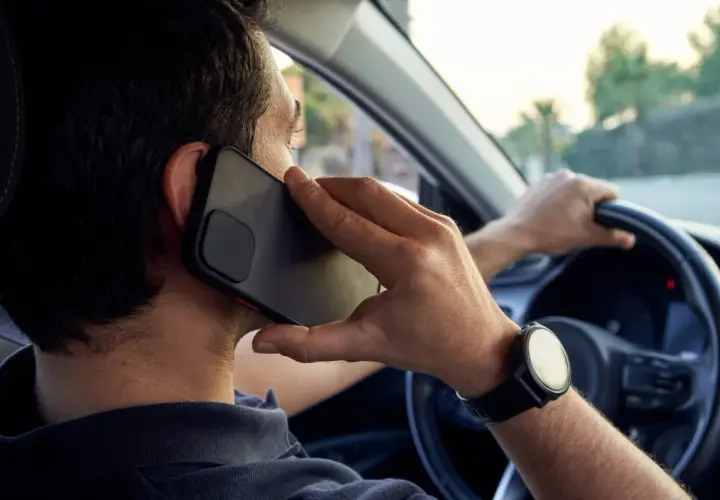 Hombre hablando por teléfono mientras conduce, una acción que puede llevar a conducir de forma temeraria.