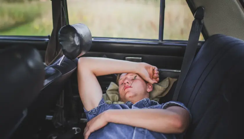 Joven descansando en el asiento trasero de un coche, demostrando que se puede dormir en el coche.