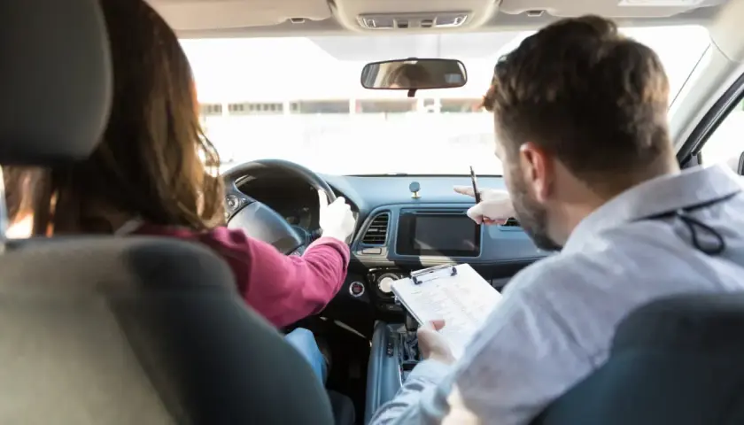 Instructor de autoescuela revisa notas mientras enseña a conducir. ¿Cuánto gana un profesor de autoescuela?