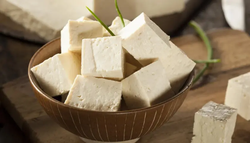 Tofu en cubos en un tazón, con bloques enteros al fondo. Aunque dicen que el tofu engorda, es un alimento versátil.