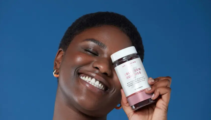 Mujer sonriente con un frasco de gomitas de colágeno para la piel, que prometen una piel radiante.