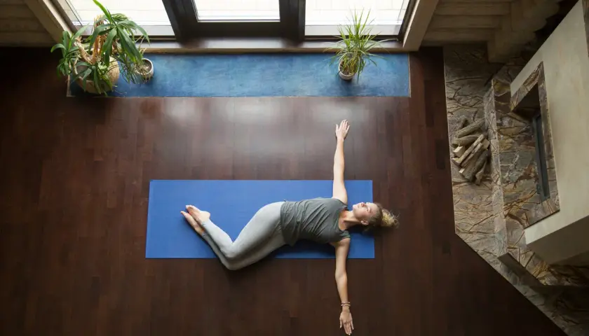 Mujer realizando ejercicios de espalda en casa, estirando su cuerpo sobre una esterilla azul.