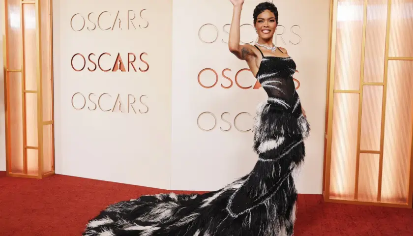 Una mujer saluda en la alfombra roja de los Oscars, luciendo un espectacular vestido negro con plumas.