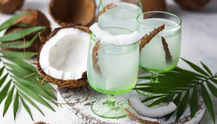 Refrescante agua de coco servida en copas verdes, decoradas con trozos de coco y hojas de palma.