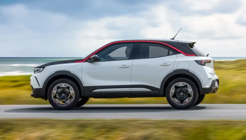 Opel Mokka blanco con detalles rojos, conduciendo por la costa. Las opiniones sobre este coche son muy positivas.