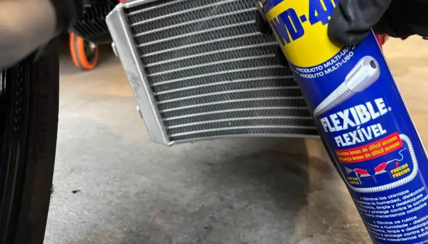 Mano enguantada usa spray WD-40 para limpiar radiador coche.