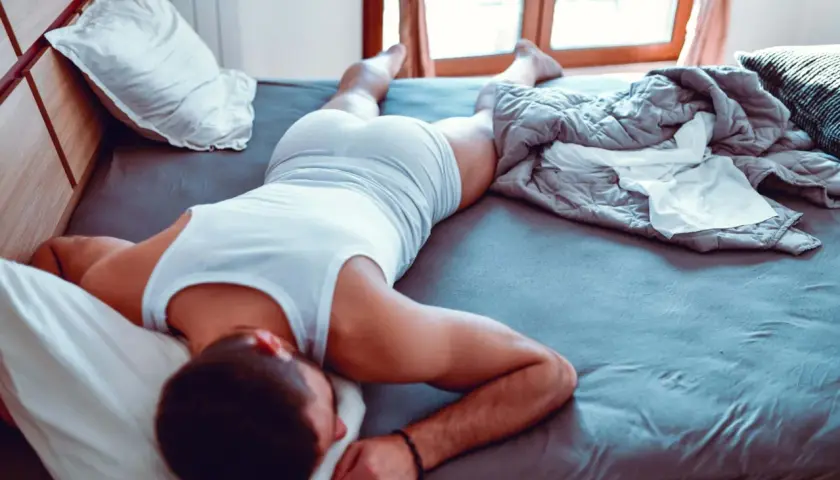 Hombre durmiendo en la cama, con una camiseta blanca y pantalones cortos. Se siente cómodo, es bueno dormir sin ropa interior.