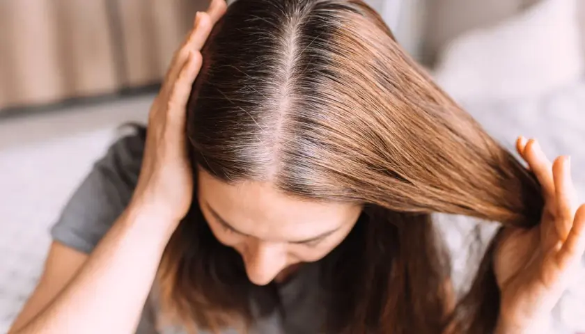 Una joven se toca el cabello, mostrando mechones grises. Se pregunta: "porque me salen canas si soy joven".