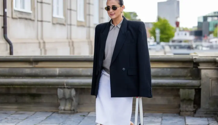 Mujer con blazer negro, falda blanca y bolso, un look que se lleva este otoño.