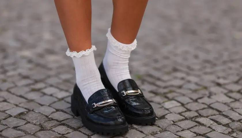 Mocasines negros con detalle de cadena y calcetines blancos con volantes. Un look moderno y chic.