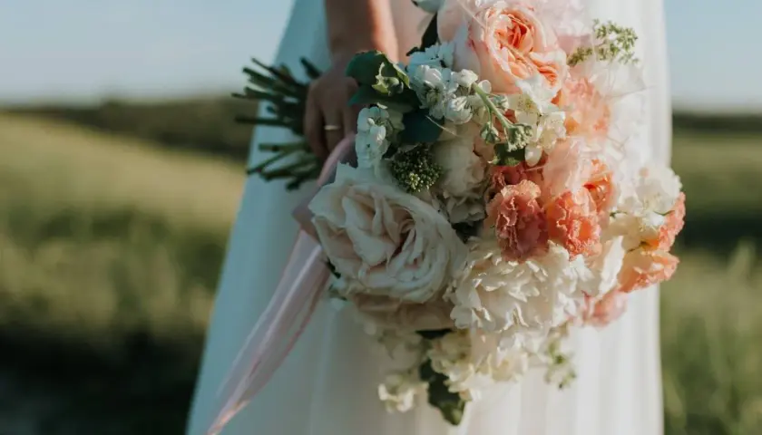 Novia con ramo de flores en tonos pastel, la última tendencia en ramos de novia, con cintas rosas cayendo.