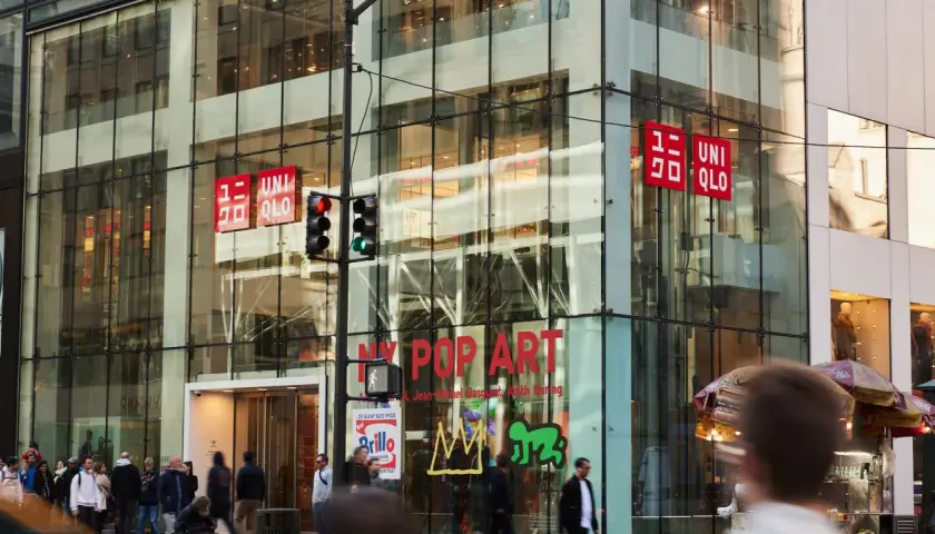 Edificio de cristal con letreros rojos de UNIQLO. La tienda, de origen japonés, se encuentra en una calle concurrida.