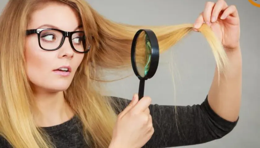 Mujer con gafas examina su cabello rubio con lupa, preocupada porque no me crece el pelo.