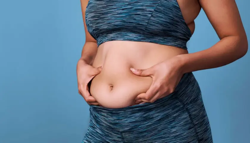 Mujer de 50 años se pellizca el abdomen, buscando perder grasa abdominal.
