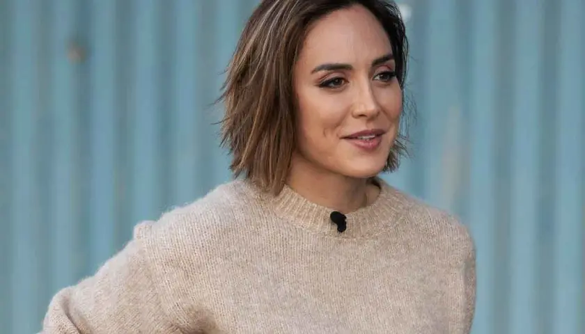 Mujer con un moderno corte de pelo bob, luciendo un suéter beige y una sonrisa amable.