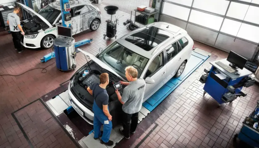 Técnicos revisan el motor de un coche de gasolina en un taller. El mantenimiento del coche es esencial.