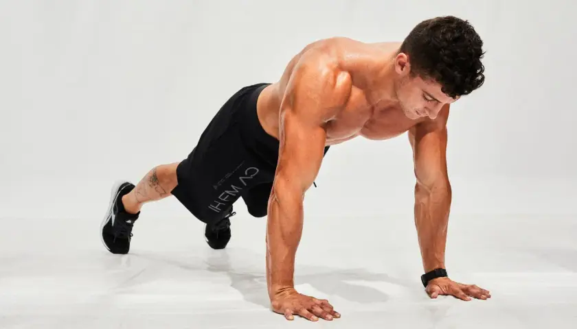 Hombre haciendo flexiones en posición de plancha, listo para un entrenamiento de hiit en casa.
