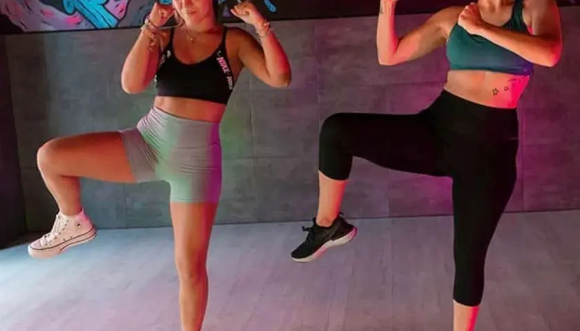 Dos mujeres en ropa deportiva entrenan con las rodillas levantadas, demostrando que el baile es un deporte.