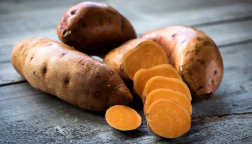Boniato entero y en rodajas sobre madera. Descubre los beneficios del boniato para adelgazar y una dieta saludable.