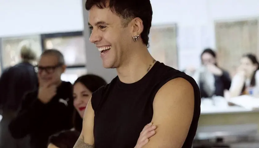 Luis de Javier diseñador, sonriente y con los brazos cruzados, rodeado de gente en un taller.
