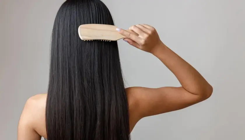 Mujer peinando su largo y oscuro cabello con un cepillo de madera, un gesto clave para saber como nutrir el pelo y mantenerlo sano y brillante.