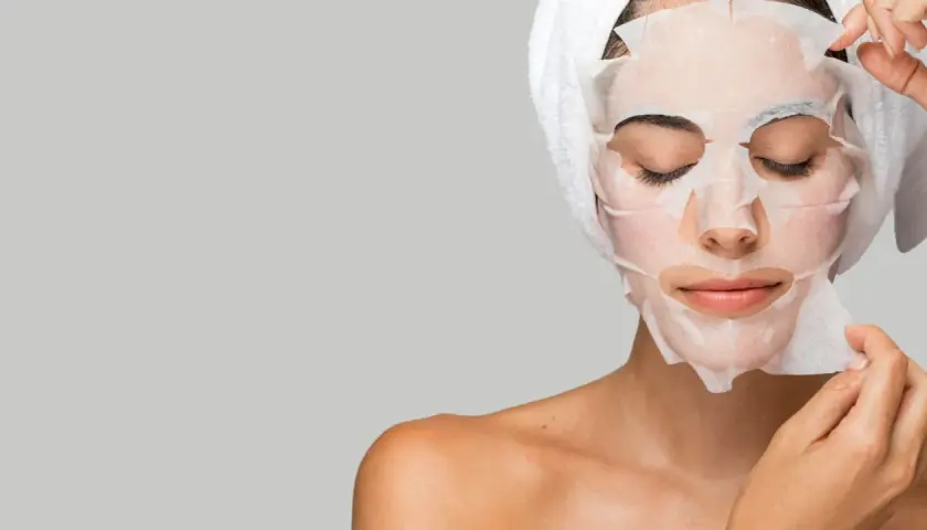 Mujer aplicándose mascarillas hidratantes pelo, con toalla en la cabeza.