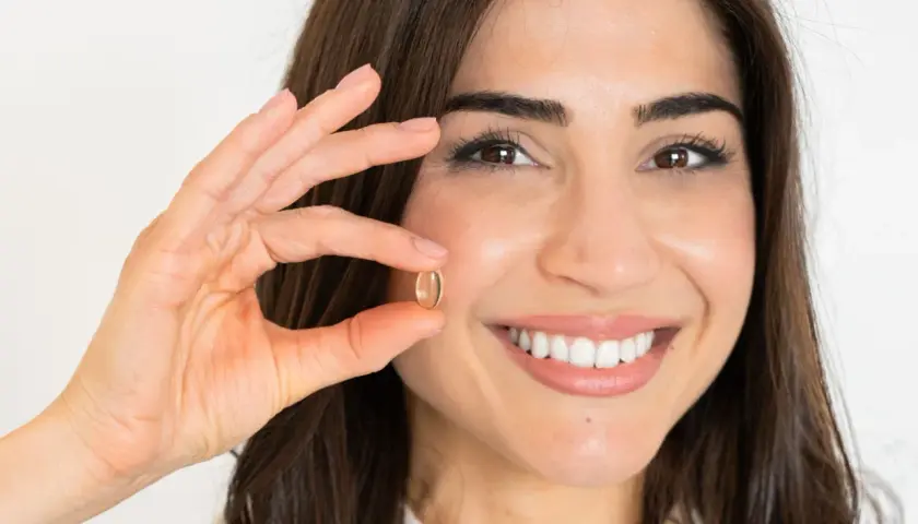 Mujer sonriente muestra una cápsula de omega 7, un aliado para quienes buscan adelgazar de forma natural.