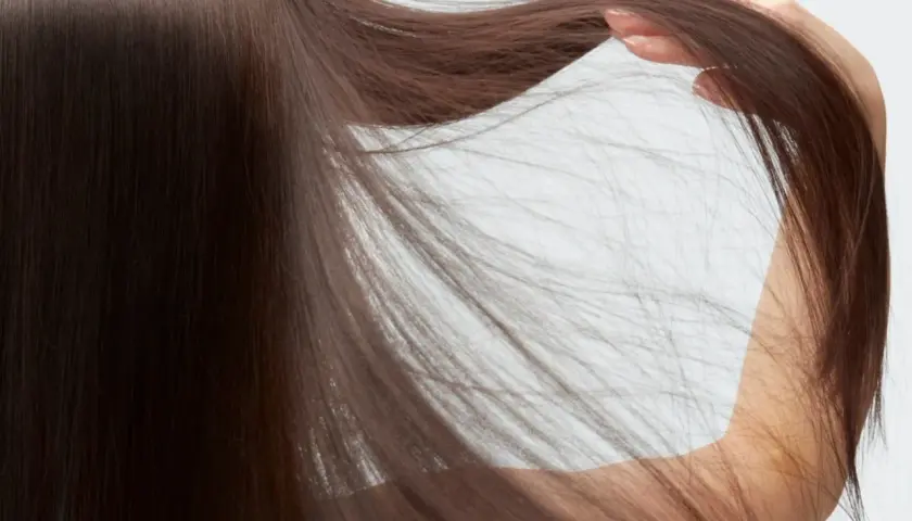 Detalle de pelo fino y escaso de mujer, con mechones sueltos que caen sobre su brazo.