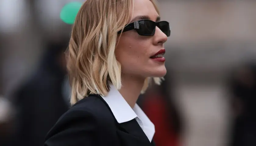 Mujer con melena corta rubia, gafas de sol y traje negro. Cortes de pelo melena corta modernos y chic.