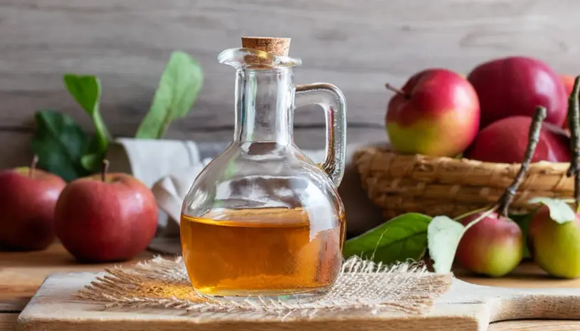Botella de vidrio con vinagre de sidra de manzana, rodeada de manzanas rojas y verdes frescas.
