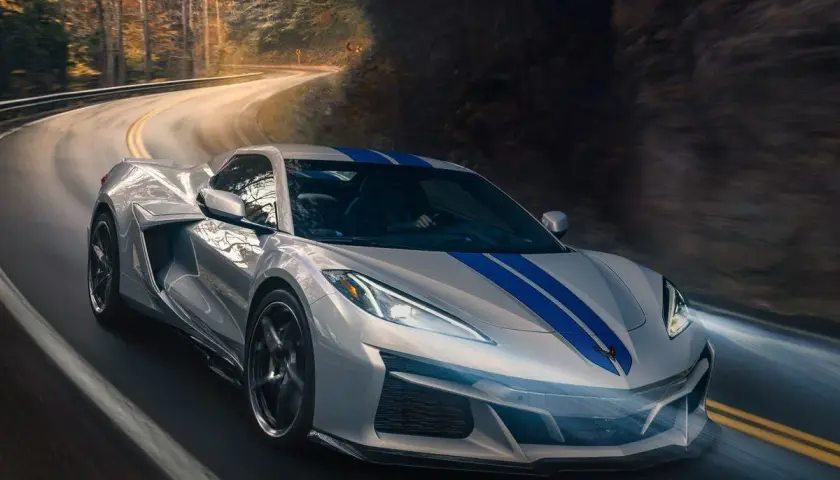 Un deportivo plateado con franjas azules recorre una carretera sinuosa entre árboles. Podría ser el mejor coche del mundo.