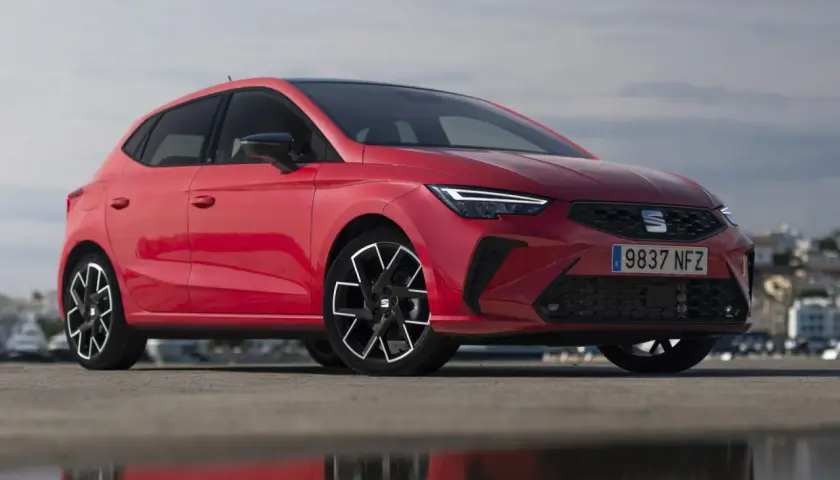 Un Seat Ibiza rojo vibrante, uno de los modelos más icónicos, posa con estilo frente a un paisaje urbano.