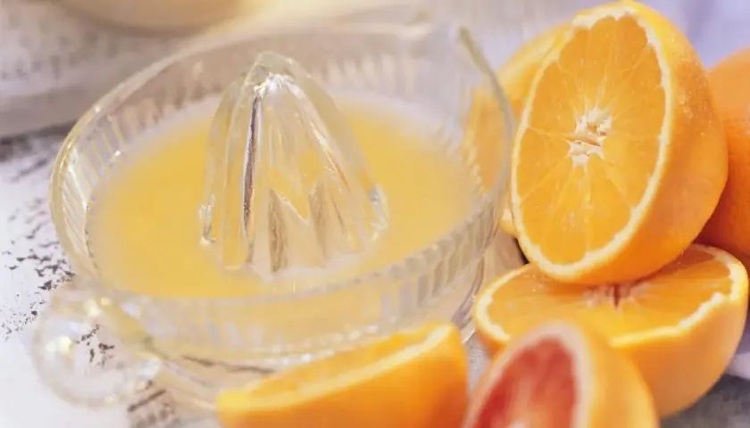 Exprimiendo naranjas frescas en un exprimidor de vidrio. El zumo de naranja natural recién hecho, listo para disfrutar.