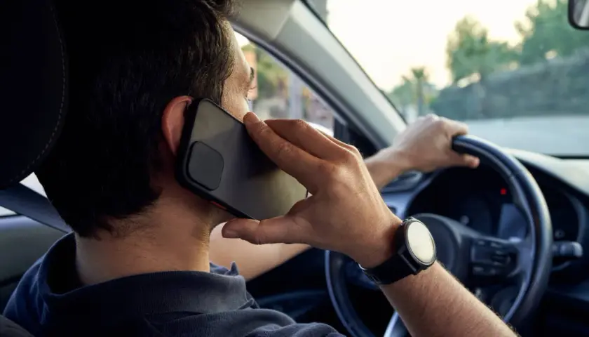 Hombre hablando por teléfono mientras conduce, una acción que puede llevar a conducir de forma temeraria.