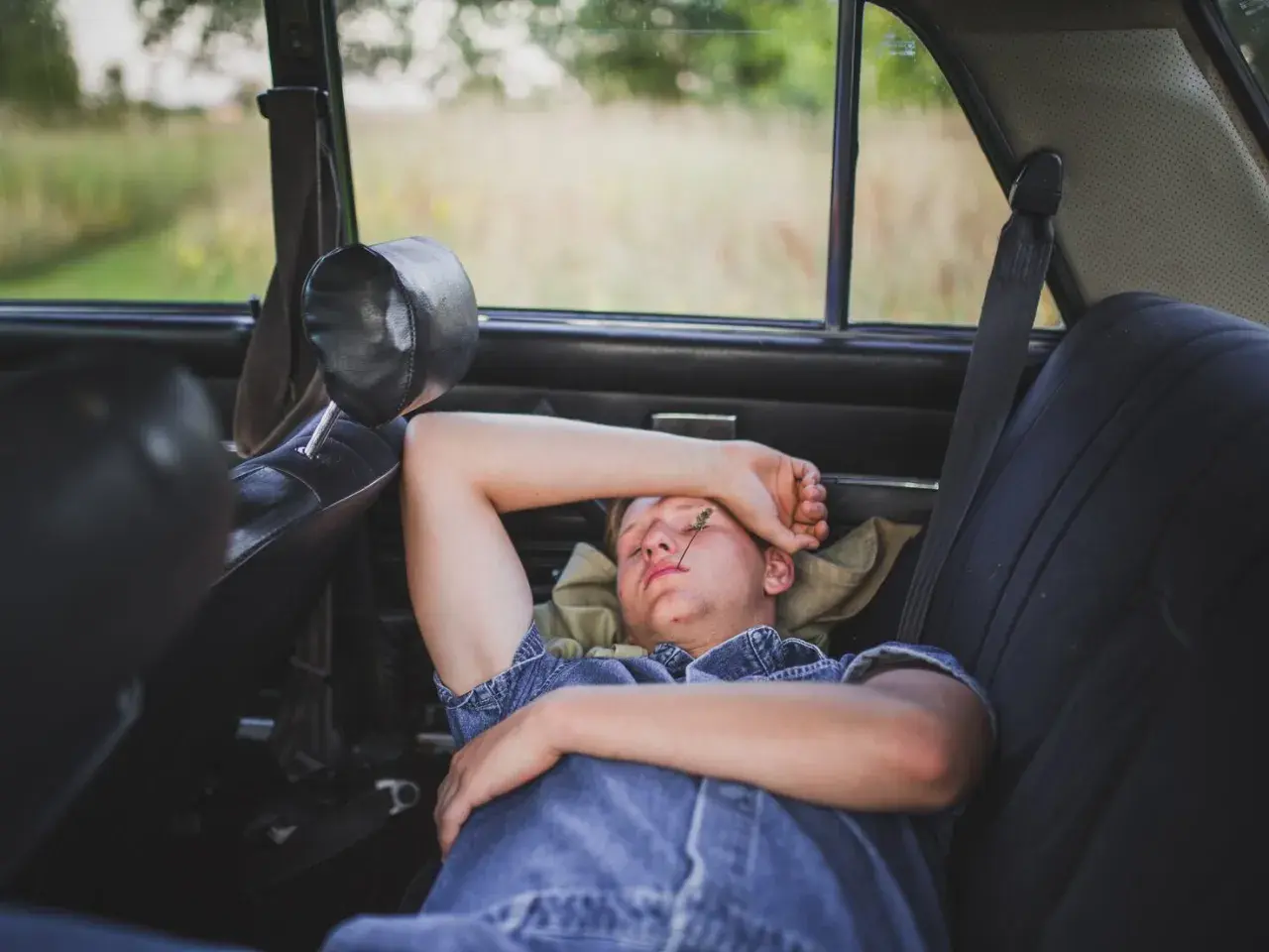 Joven descansando en el asiento trasero de un coche, demostrando que se puede dormir en el coche.
