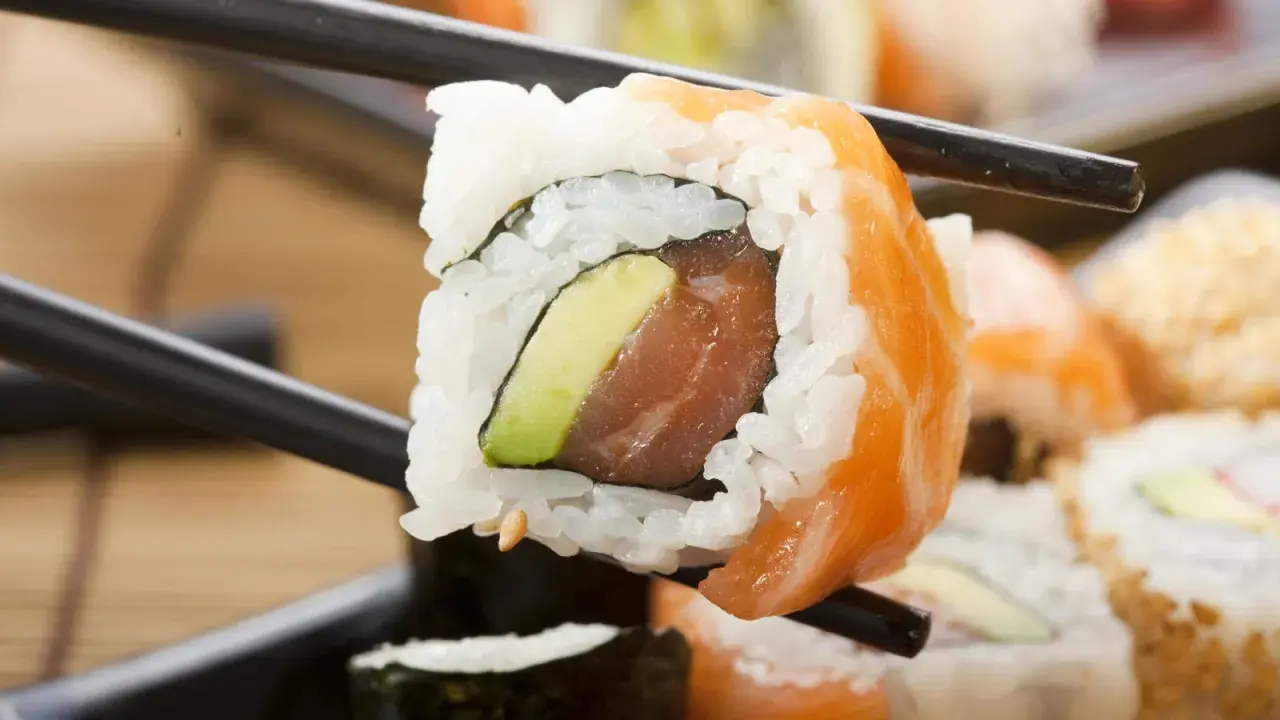 Palillos sostienen un rollo de sushi con salmón y aguacate. ¡Cuidado, el sushi engorda si no te controlas!