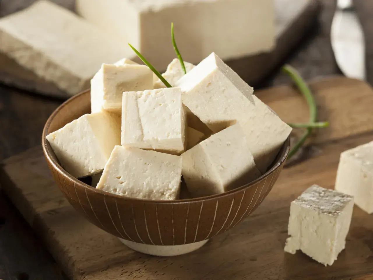 Tofu en cubos en un tazón, con bloques enteros al fondo. Aunque dicen que el tofu engorda, es un alimento versátil.