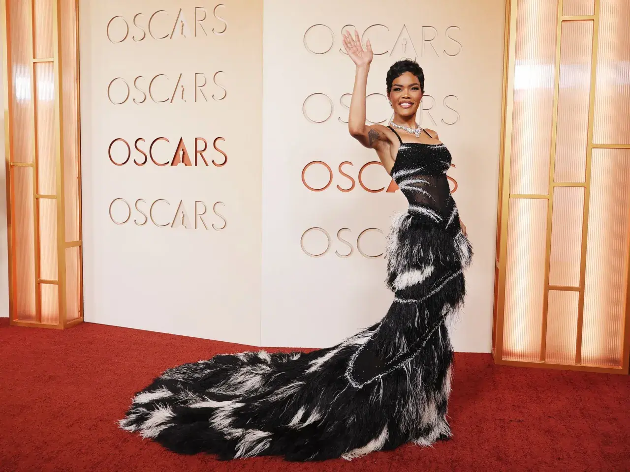 Una mujer saluda en la alfombra roja de los Oscars, luciendo un espectacular vestido negro con plumas.