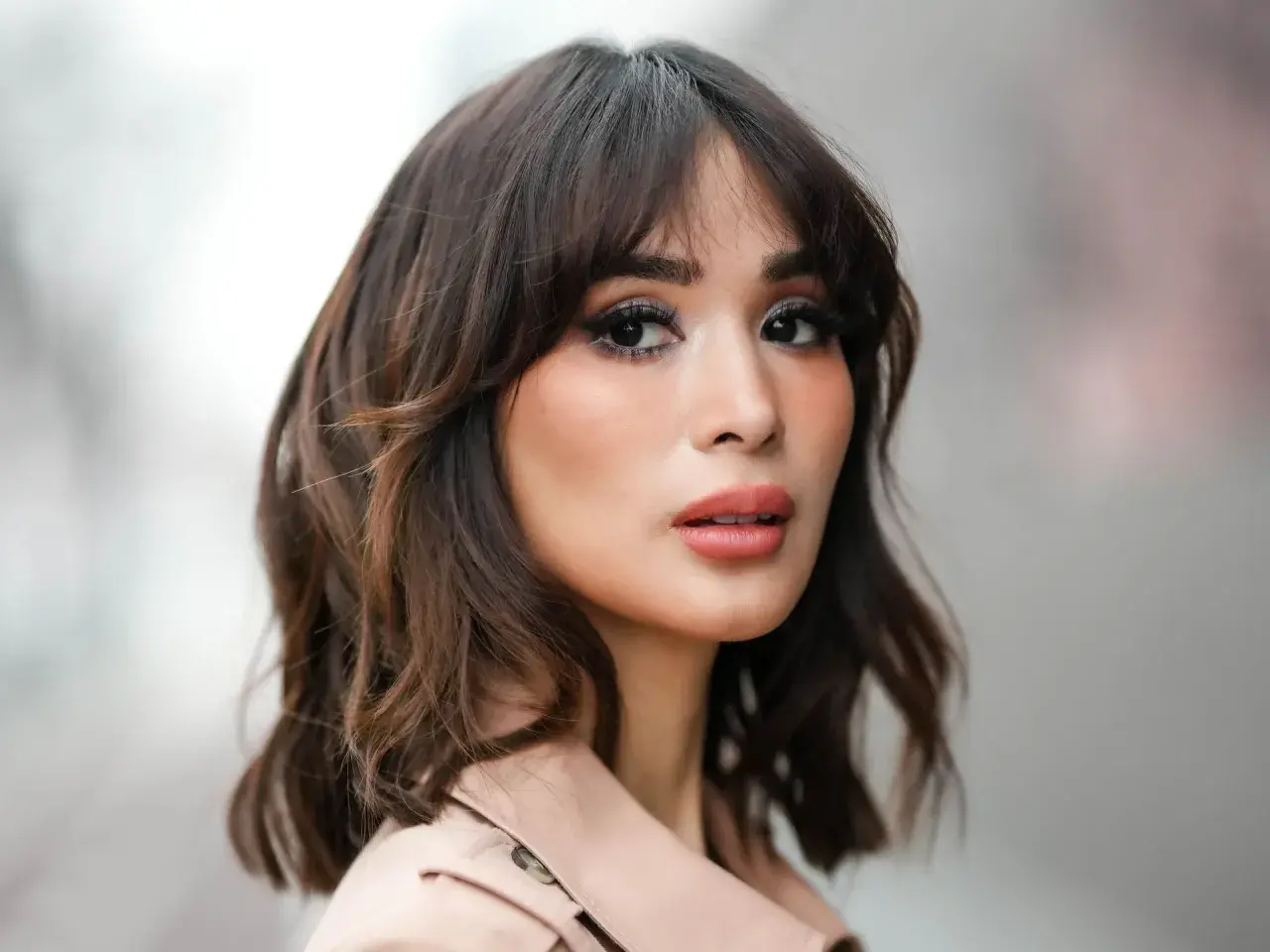 Mujer con un moderno corte wolf cut, cabello castaño ondulado y maquillaje llamativo.