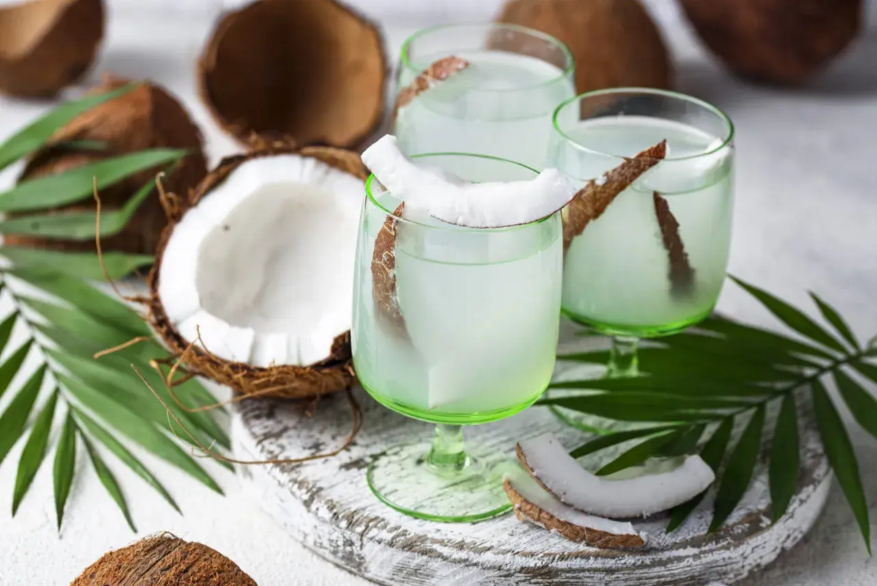 Refrescante agua de coco servida en copas verdes, decoradas con trozos de coco y hojas de palma.