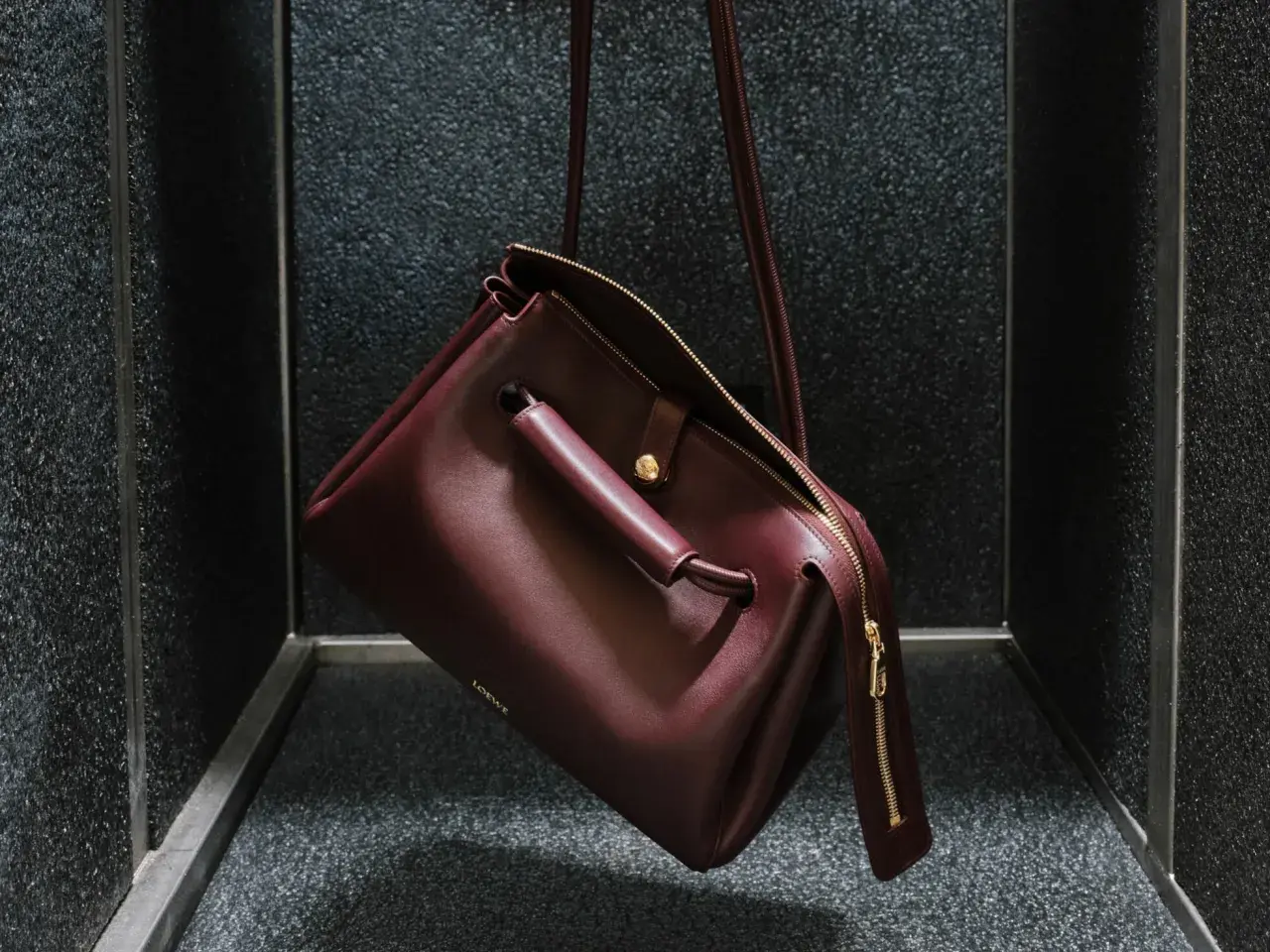 Bolso Loewe de cuero burdeos, con detalles dorados y el logo grabado. Un accesorio que evoca el lujo y la artesanía de España, de donde es Loewe.