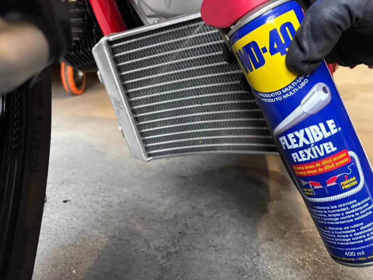 Mano enguantada usa spray WD-40 para limpiar radiador coche.