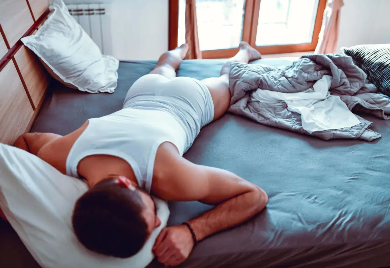 Hombre durmiendo en la cama, con una camiseta blanca y pantalones cortos. Se siente cómodo, es bueno dormir sin ropa interior.