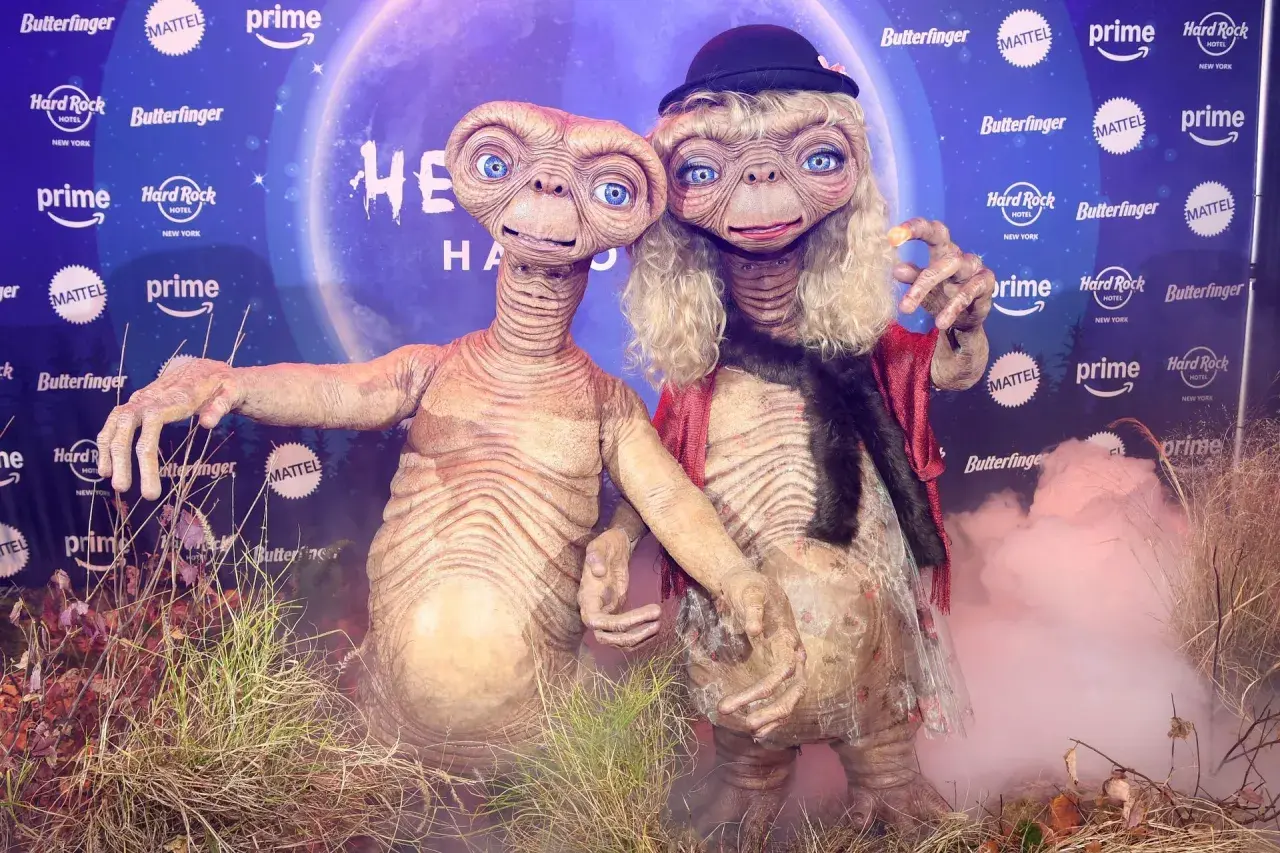 Dos E.T. disfrazados, uno con sombrero y peluca rubia, celebran Halloween. ¡Un guiño a Heidi Klum!