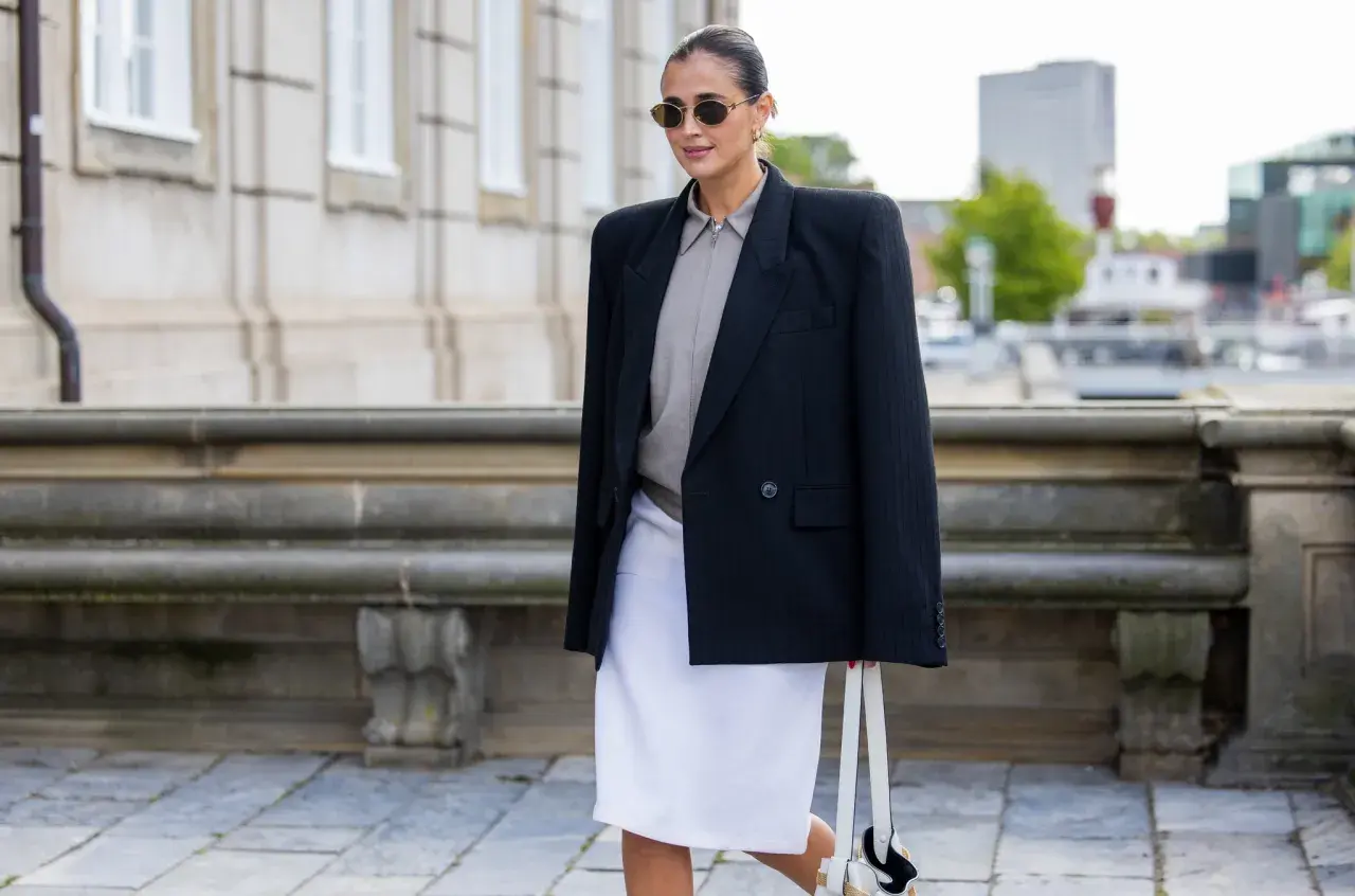 Mujer con blazer negro, falda blanca y bolso, un look que se lleva este otoño.