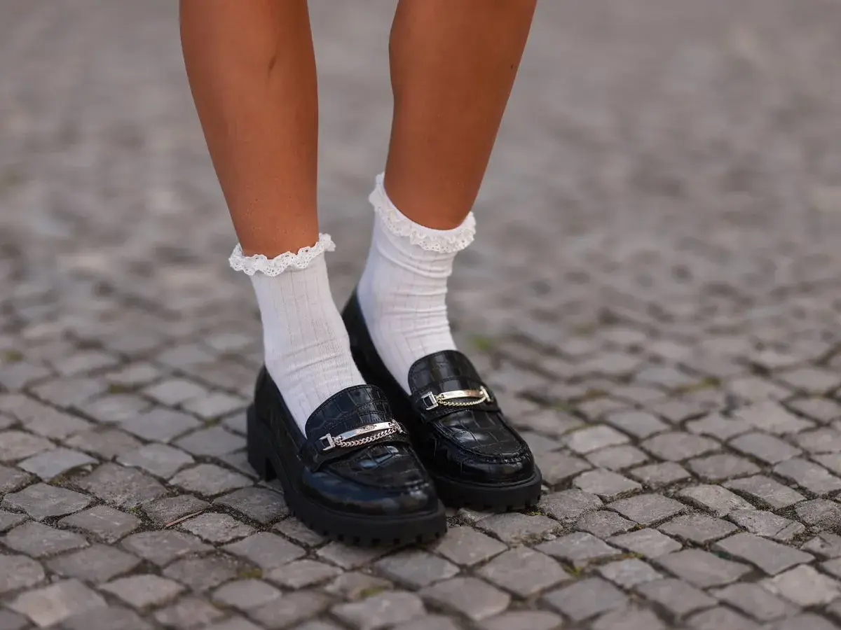 Mocasines negros con detalle de cadena y calcetines blancos con volantes. Un look moderno y chic.