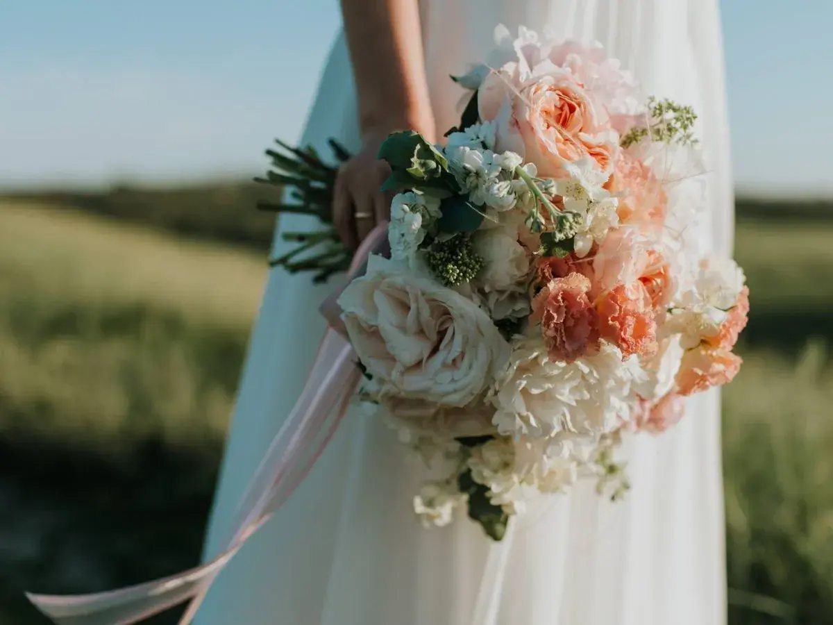 Novia con ramo de flores en tonos pastel, la última tendencia en ramos de novia, con cintas rosas cayendo.