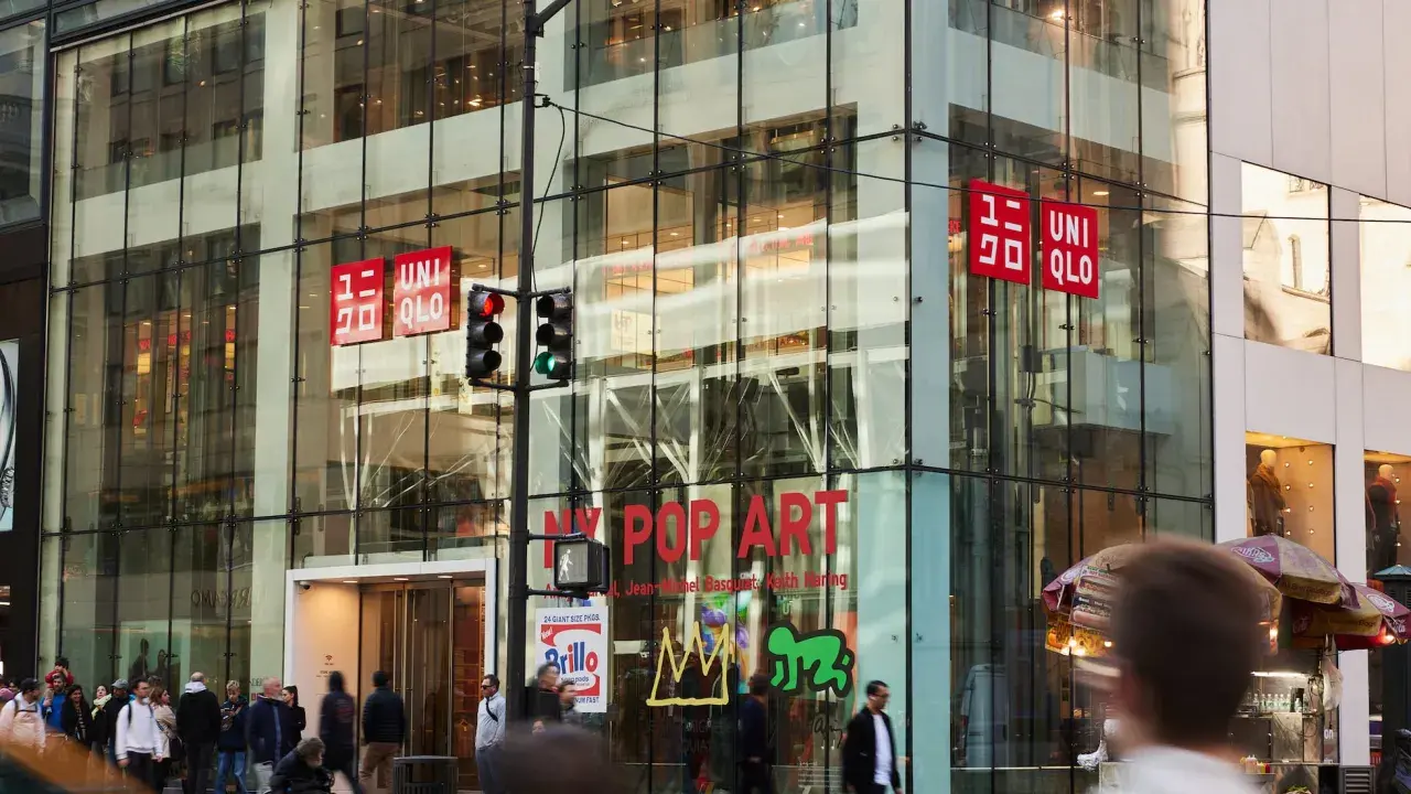 Edificio de cristal con letreros rojos de UNIQLO. La tienda, de origen japonés, se encuentra en una calle concurrida.