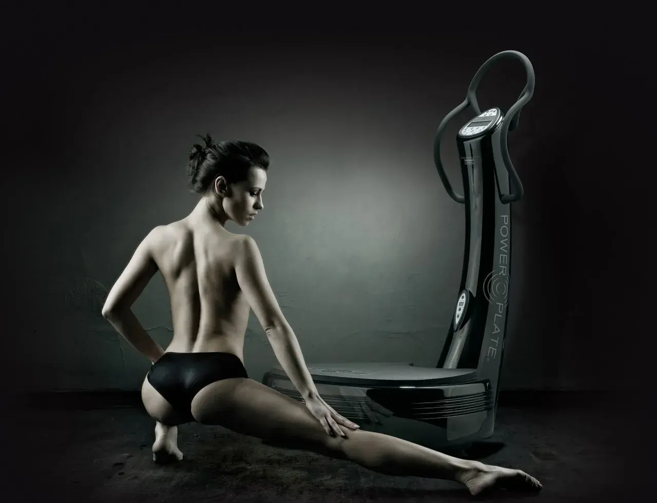 Mujer en pose de estiramiento junto a una plataforma vibratoria, destacando los plataforma vibratoria beneficios para el cuerpo.
